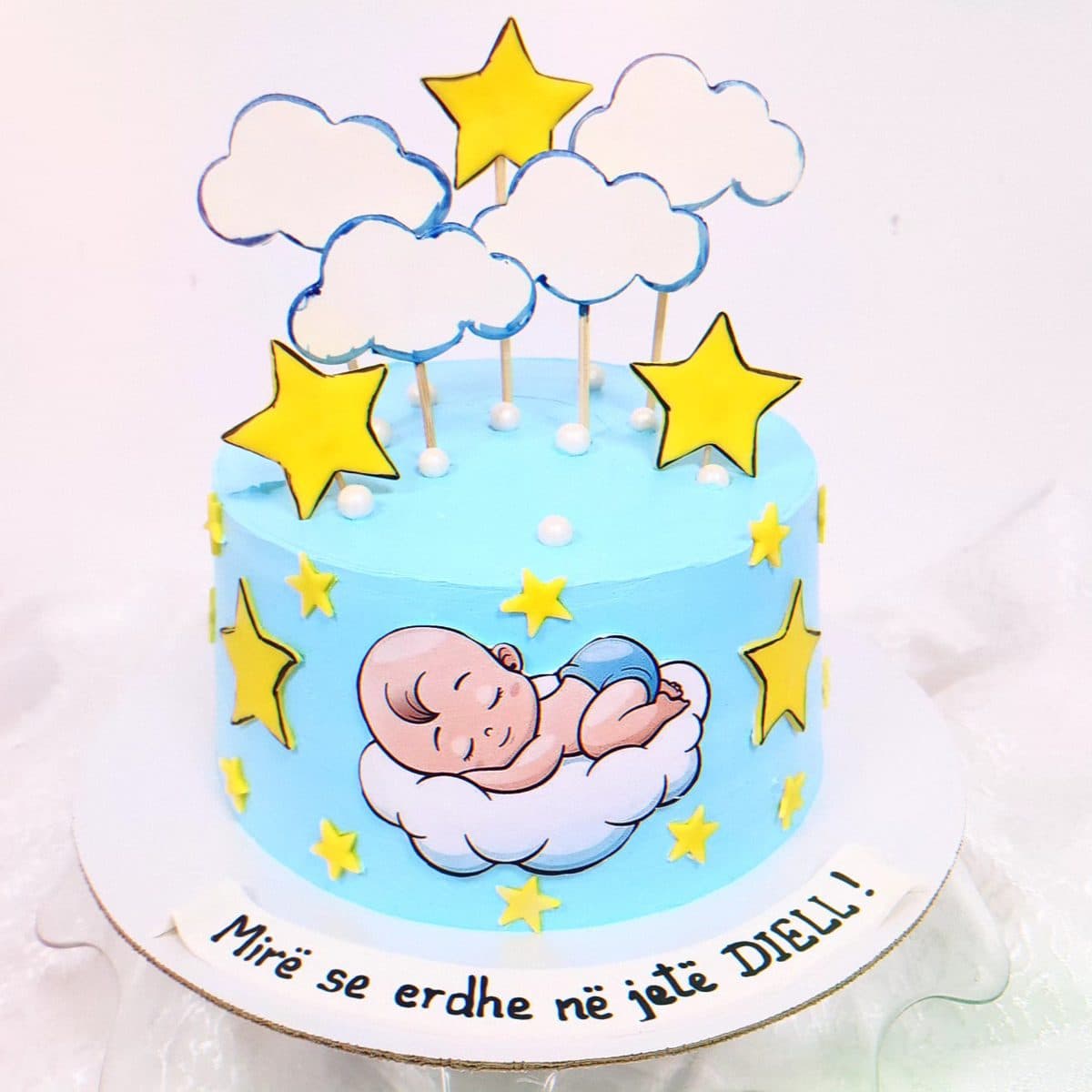 Tortë blu me re, yje dhe bebe që fle, me mbishkrimin Mirë se erdhe në jetë