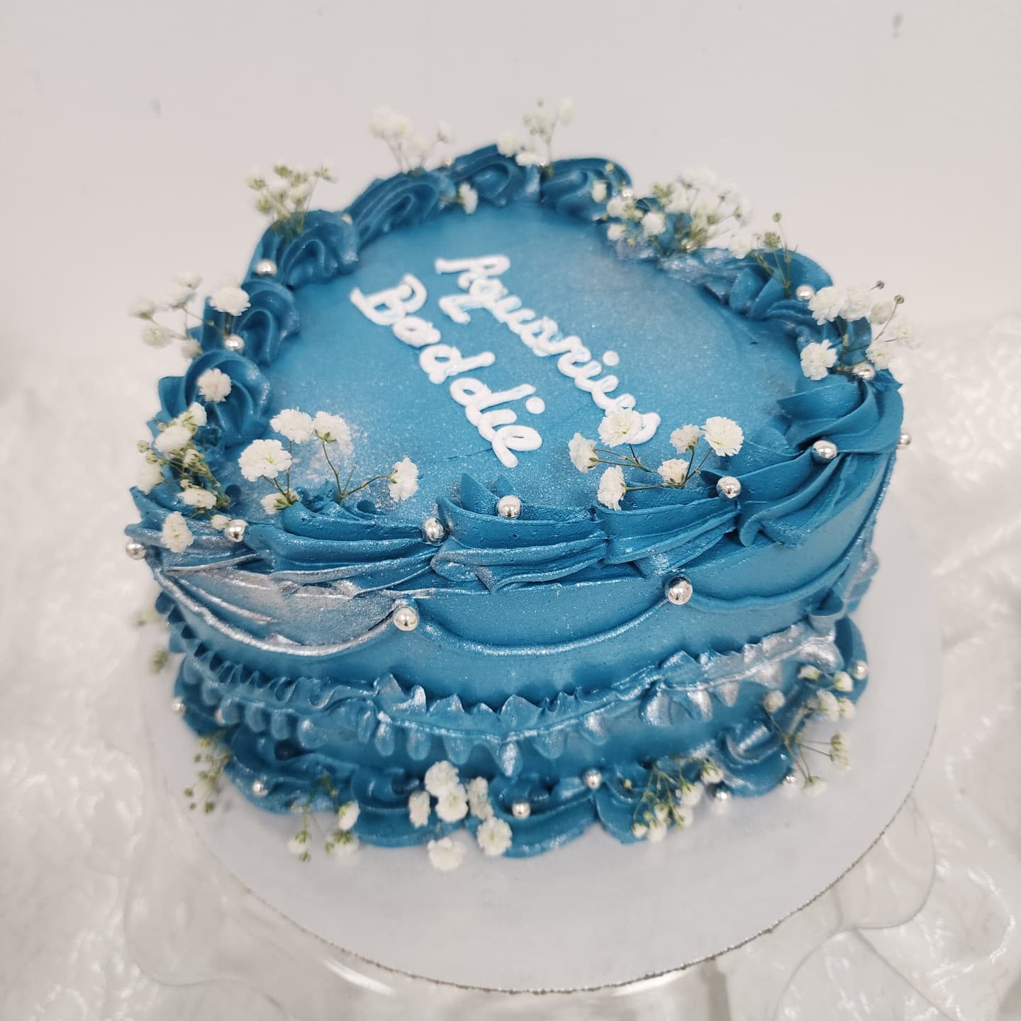 Tortë blu me lule të bardha dhe detaje argjendi