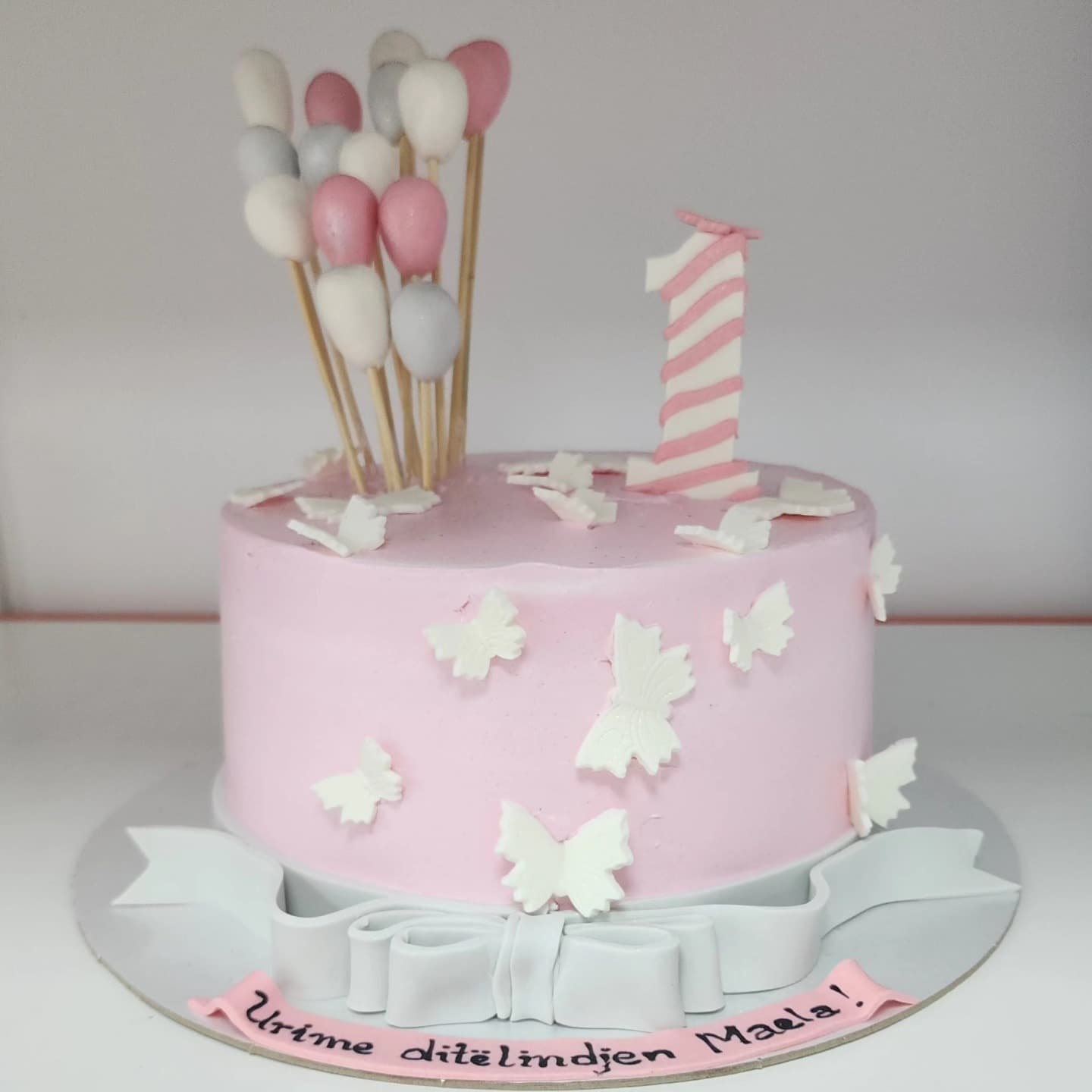 Torte rozë me flutura të bardha dhe dekor balonash për 1-vjetor
