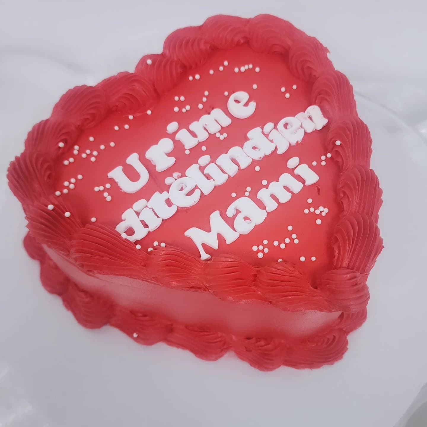 Torte në formë zemre me krem të kuq dhe detaje të bardha për ditëlindje